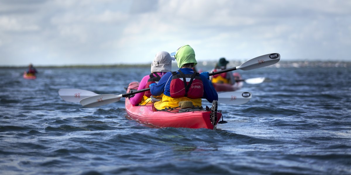 A red tandem kayak from behind with the person in the back wearing a green buff over their neck