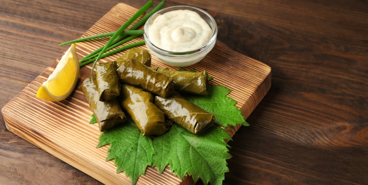 Turkish dolmas on a cutting board with a lemon wedge, chives, and yogurt sauce.