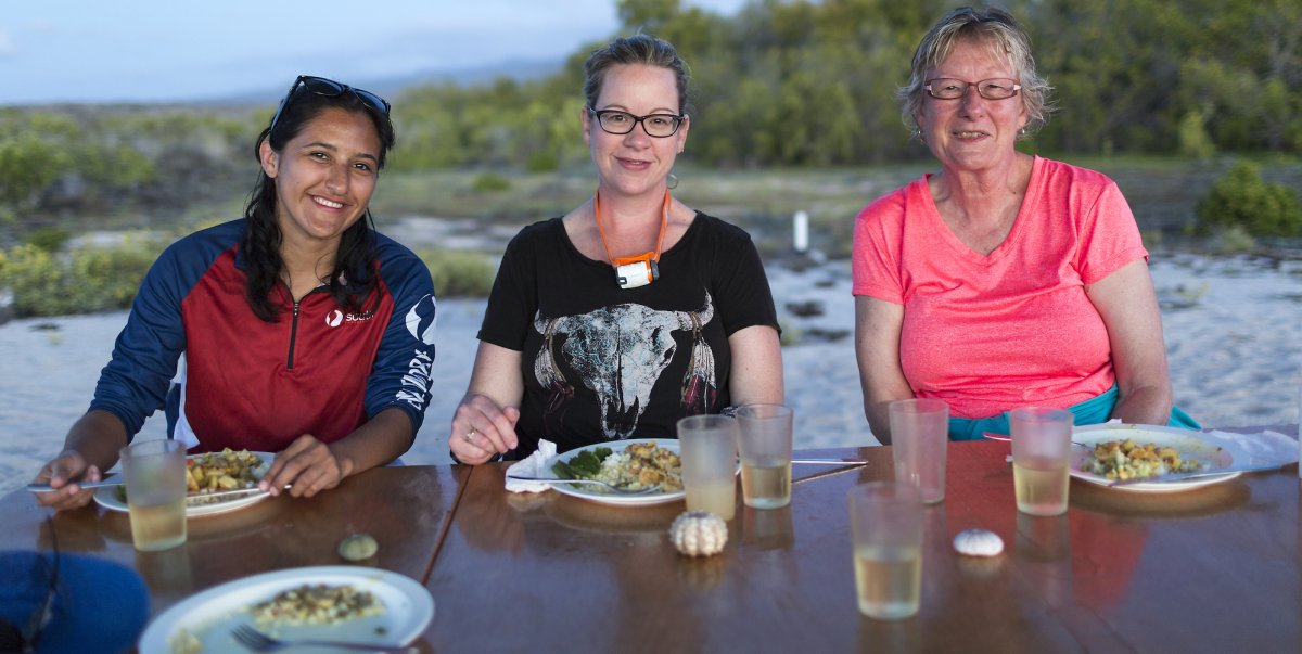 Three ladies eating a seafood and rice dinner with a side of broccoli on the beach in the Galapagos Islands