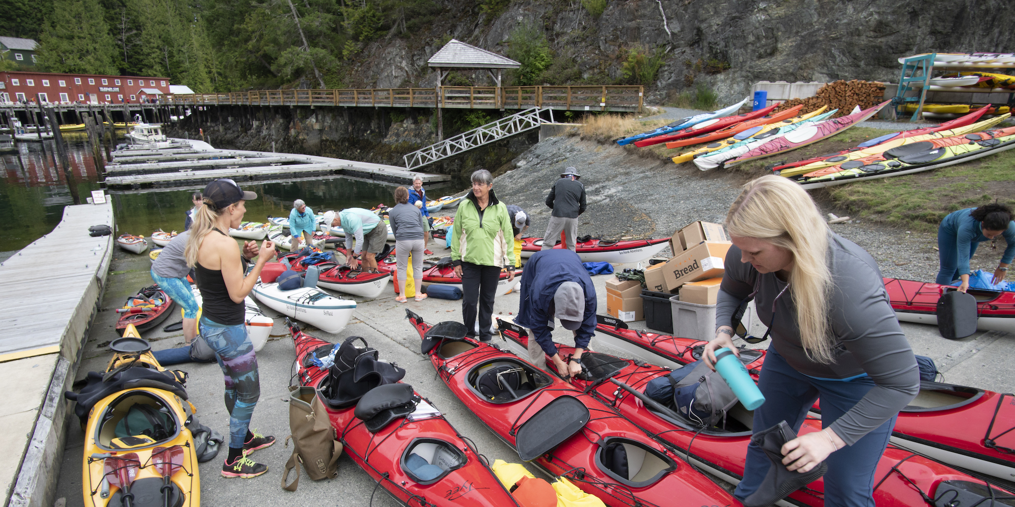 A group of sea kayakers packing their hatches and getting ready for a week on the water at a dock in British Columbia