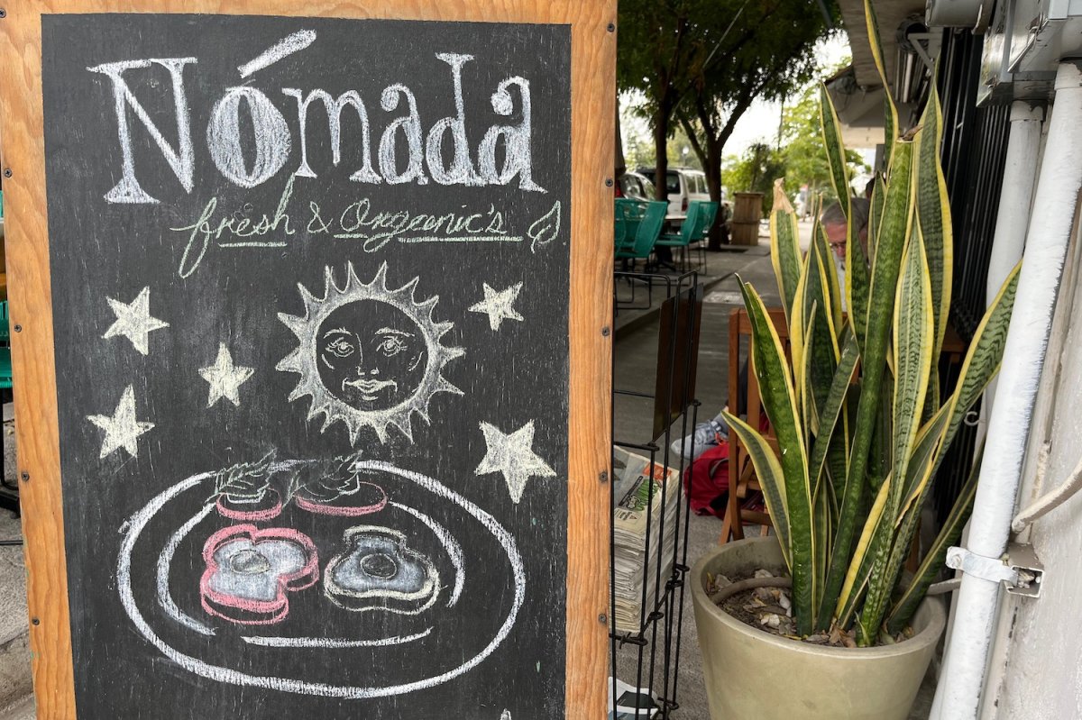 Chalkboard sign sayind Nomada Fresh and Organics with drawn plate of fried eggs and and toast next to a tall snake plant 