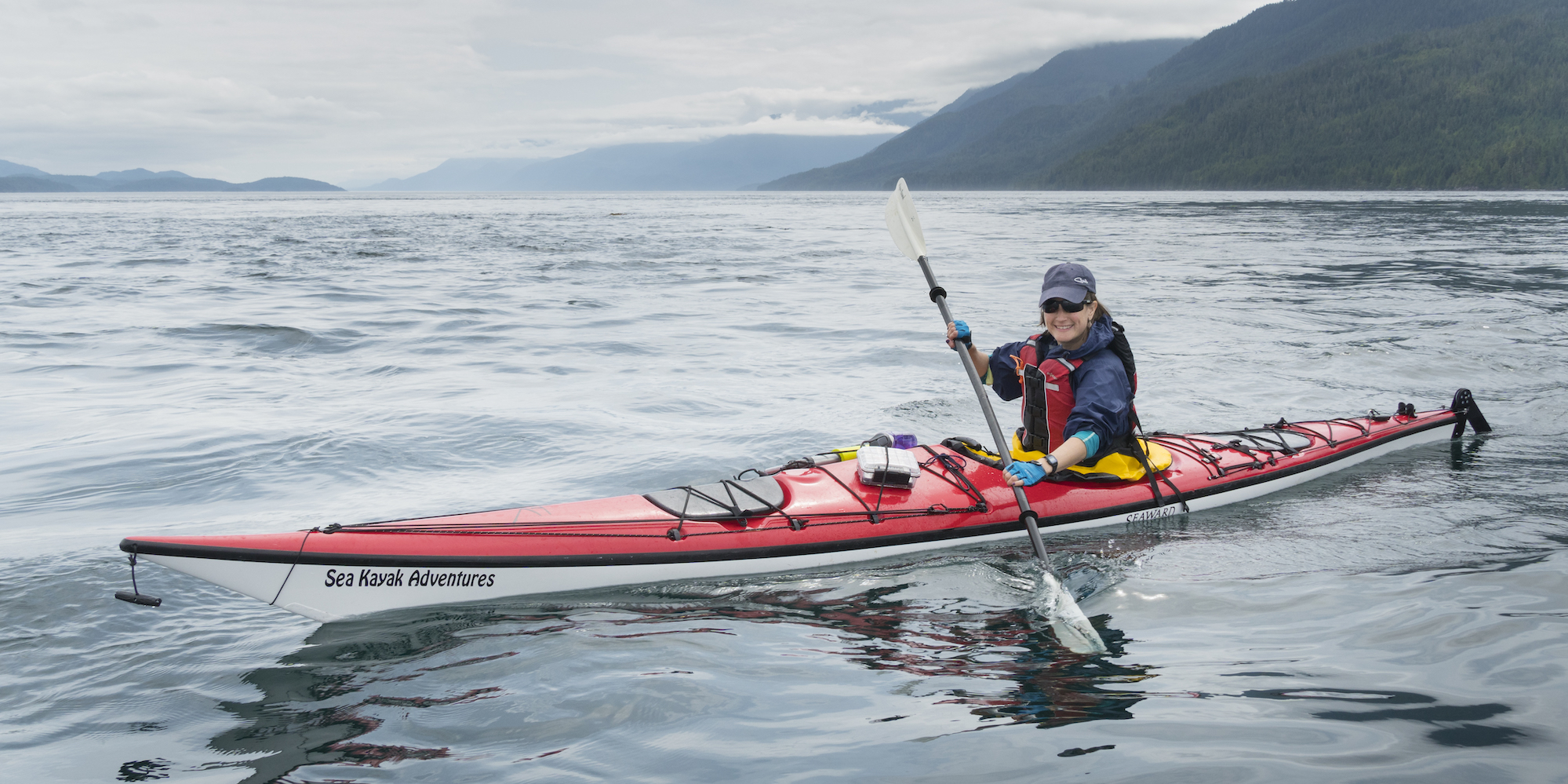 A woman in a red and white Seaward sea kayak paddling and smiling for the camera on a foggy day in British Columbia