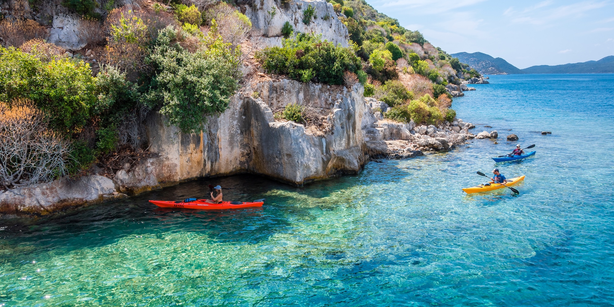 A group of sea kayakers paddling outside of the coast of Turkey in the clear waters.