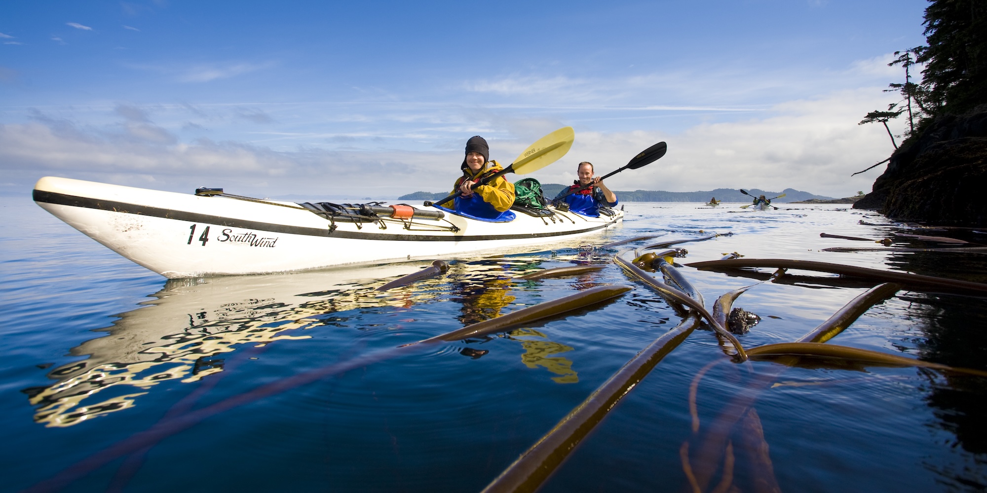 Two sea kayakers smiling as they paddle through the water in BC.