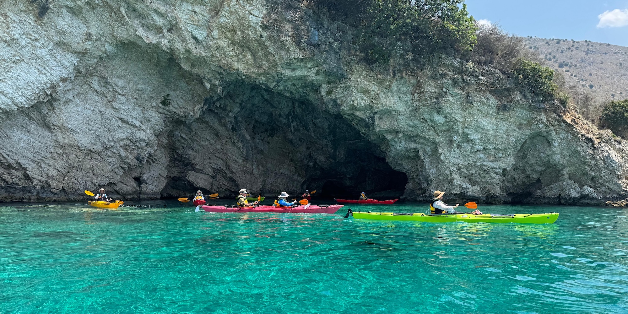 Guests paddle colorful sea kayaks into a hidden sea cave along the crystal clear Adriatic coastline.