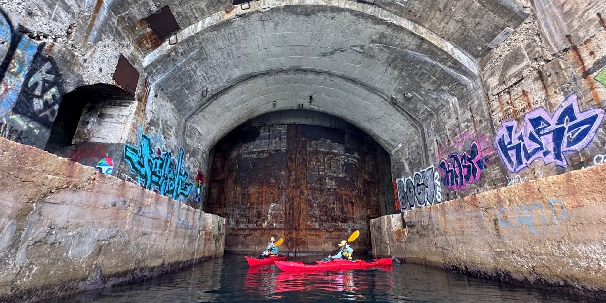 Sea kayakers explore a former submarine tunnel carved into the coastline during a guided kayaking adventure in Croatia.