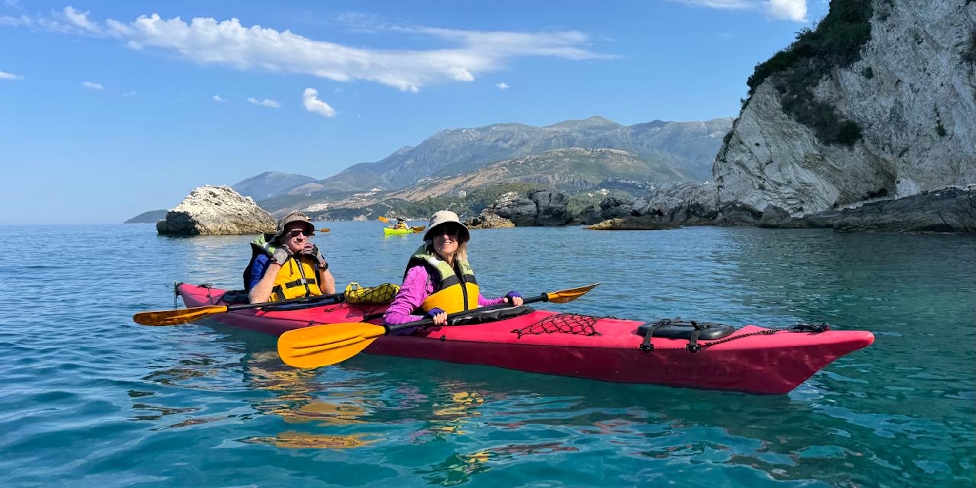 Guests paddle sea kayaks beneath rugged coastal cliffs on a guided kayaking trip through Croatia, Montenegro, and Albania.