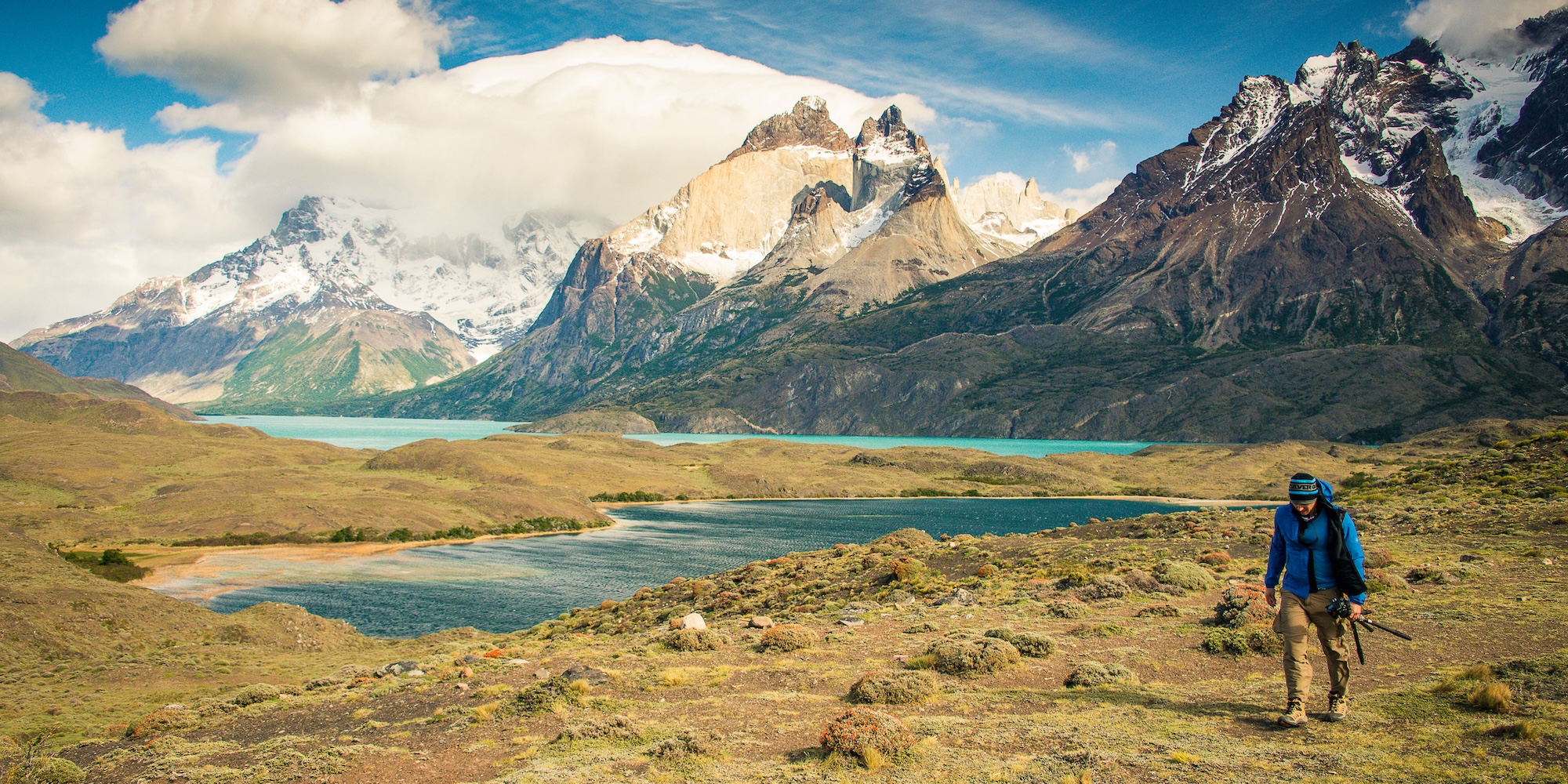 Hiker walking a trail in Torres del Paine National Park, surrounded by lakes and dramatic mountain peaks—a reminder to train for endurance and uneven terrain.