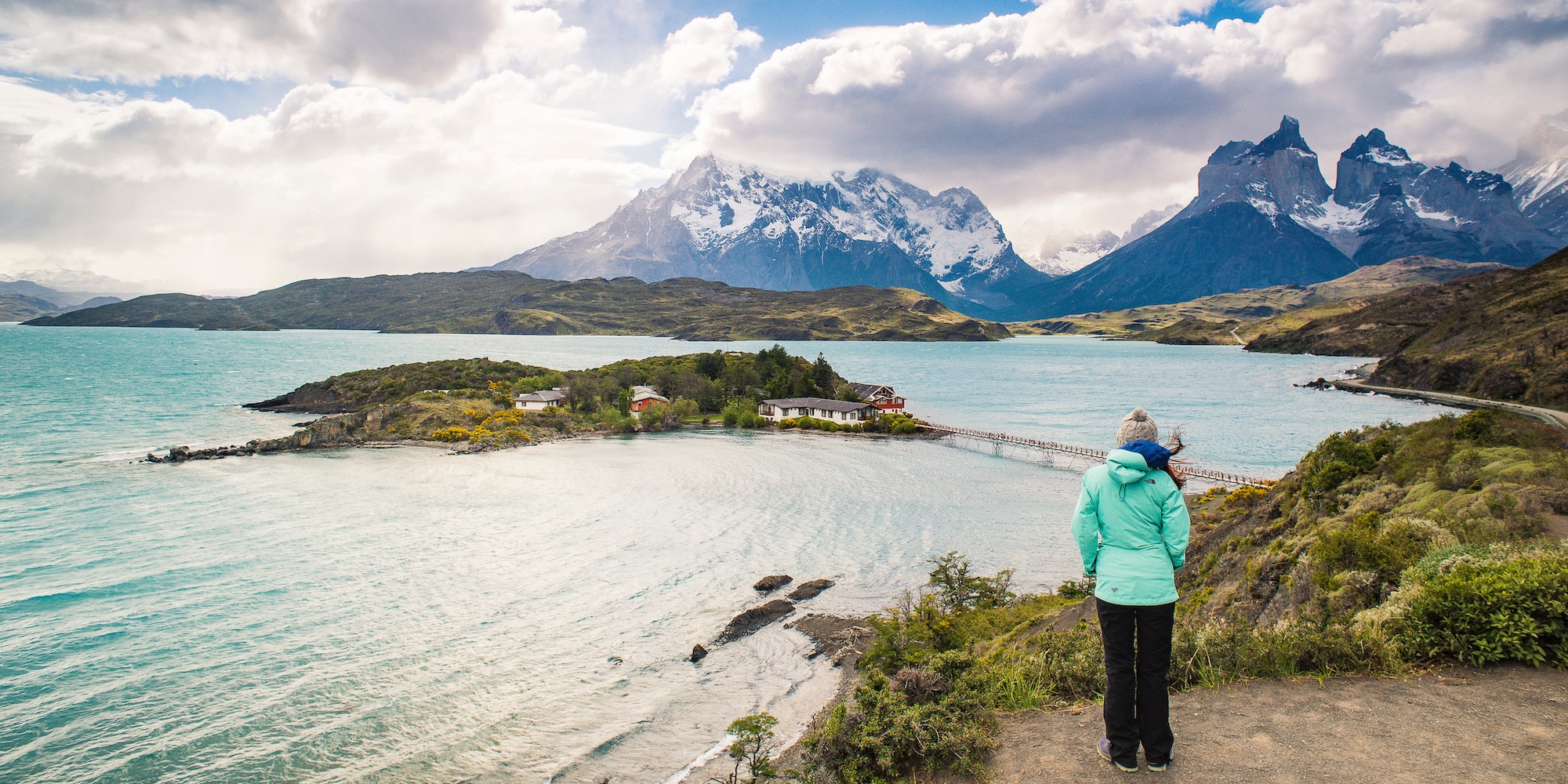 Traveler in a warm jacket overlooking a turquoise lake and jagged peaks in Torres del Paine—ideal layering clothing for changing weather in Patagonia.