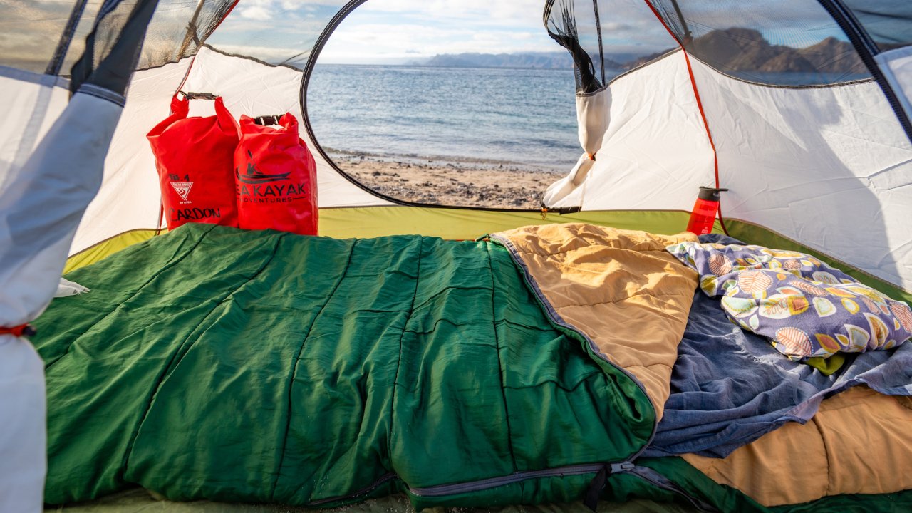 Inside of a tent with a sleeping pad, sleeping bag, dry bags, and pillow nicely set up with the ocean in the background