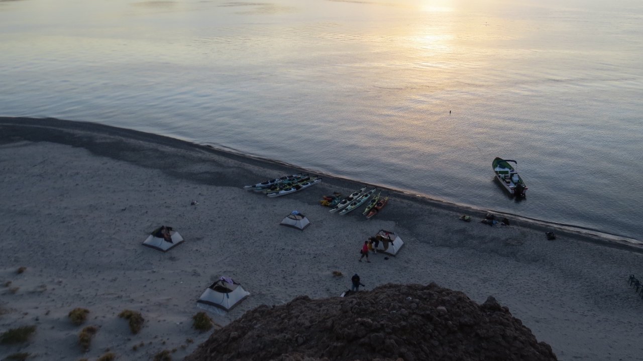 A birds eye view of tents and kayaks on a beach at sunset
