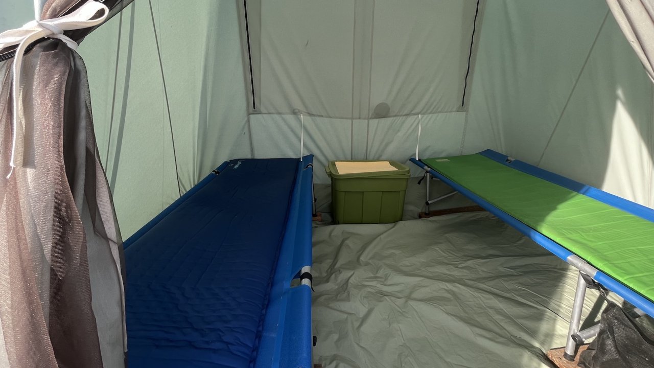 Two cots with sleeping pads set up inside of a tall canvas tent