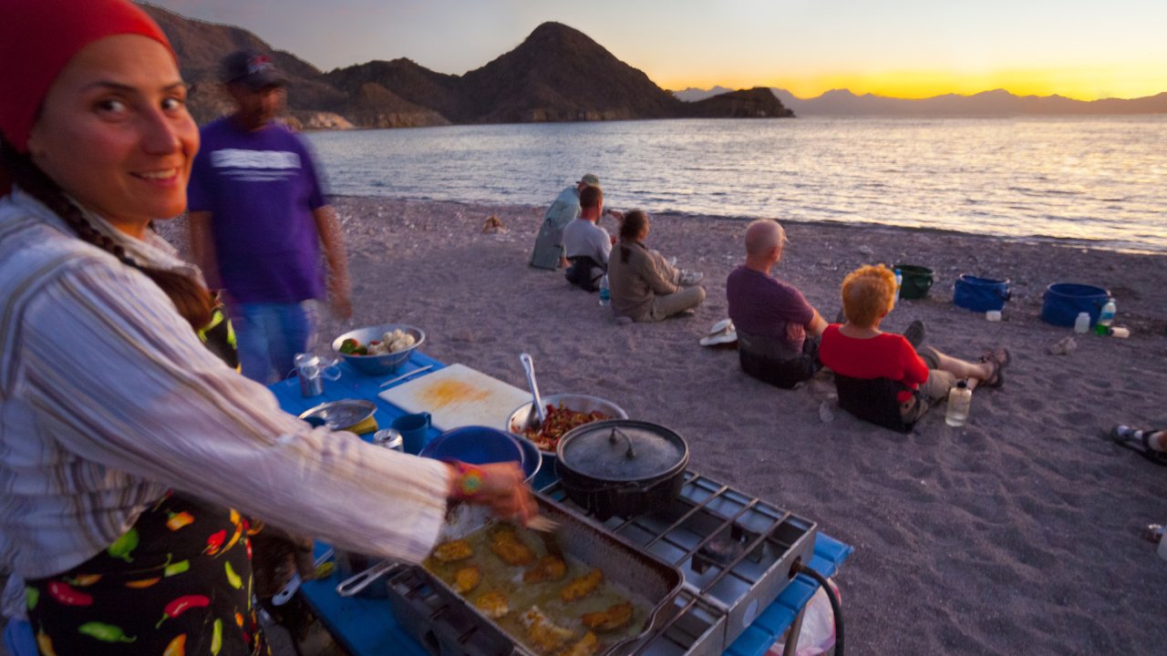 Sea Kayak Adventures guide making dinner while guests watch the sunset on the beach