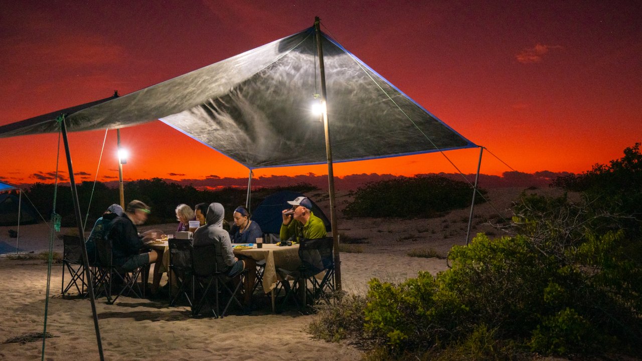 People sitting under a tent at sunset at camp in the Galapagos 