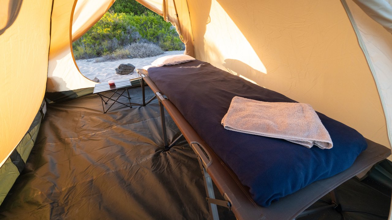 A cot, sleeping pad, and sheets inside of a canvas tent on the Galapagos Islands 