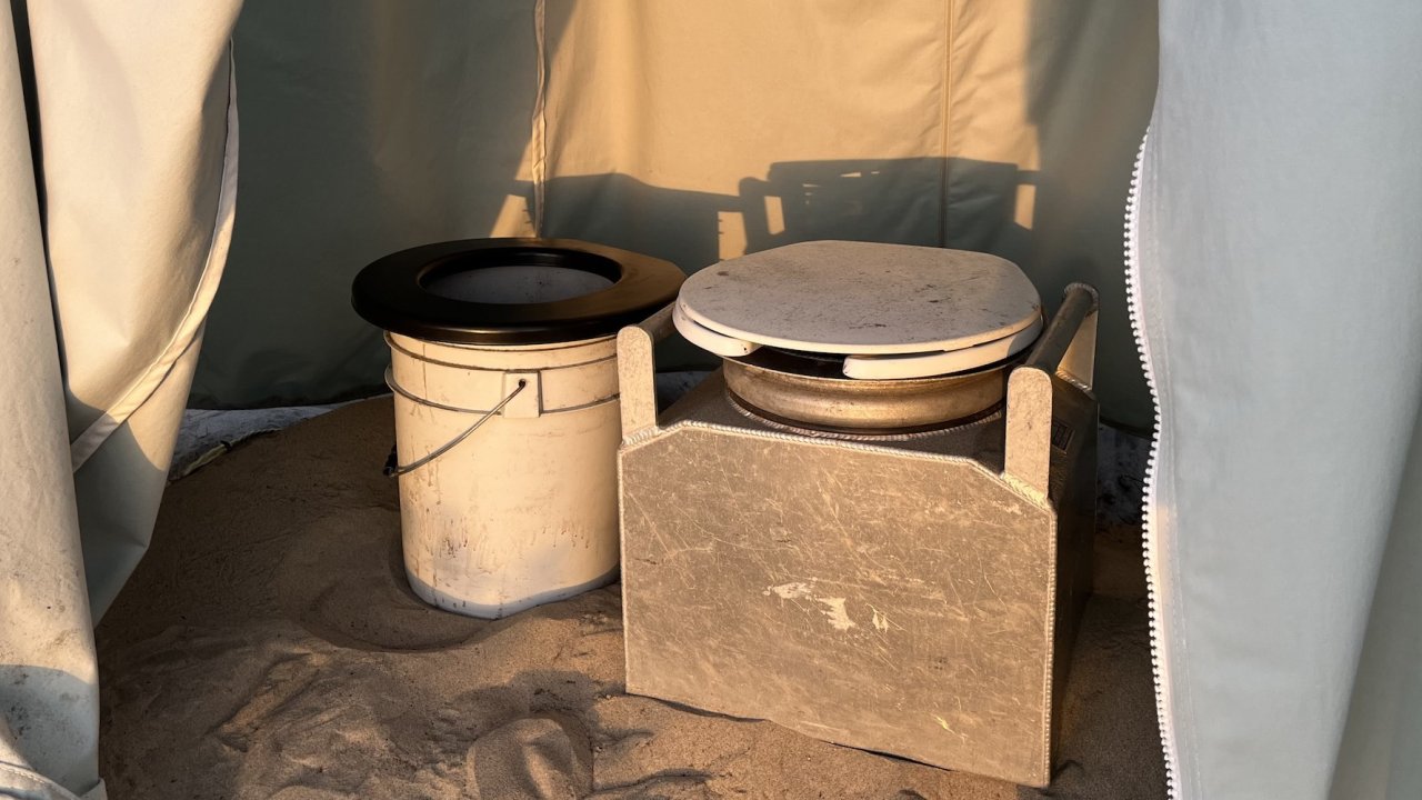 Solid waste and liquid waste buckets inside of a stand up tent in the sand while camping