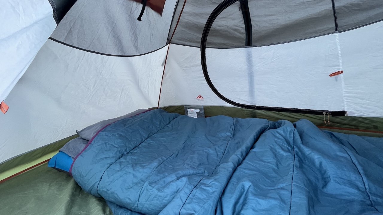 A blue inflatable sleeping pad with a blue sleeping bag inside of a tent