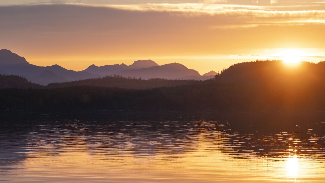 Golden sunset over calm water and forested mountains in British Columbia.