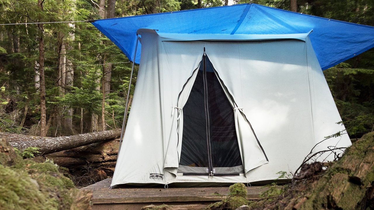 Canvas tent set on a wooden platform beneath trees at a forest camp in British Columbia.