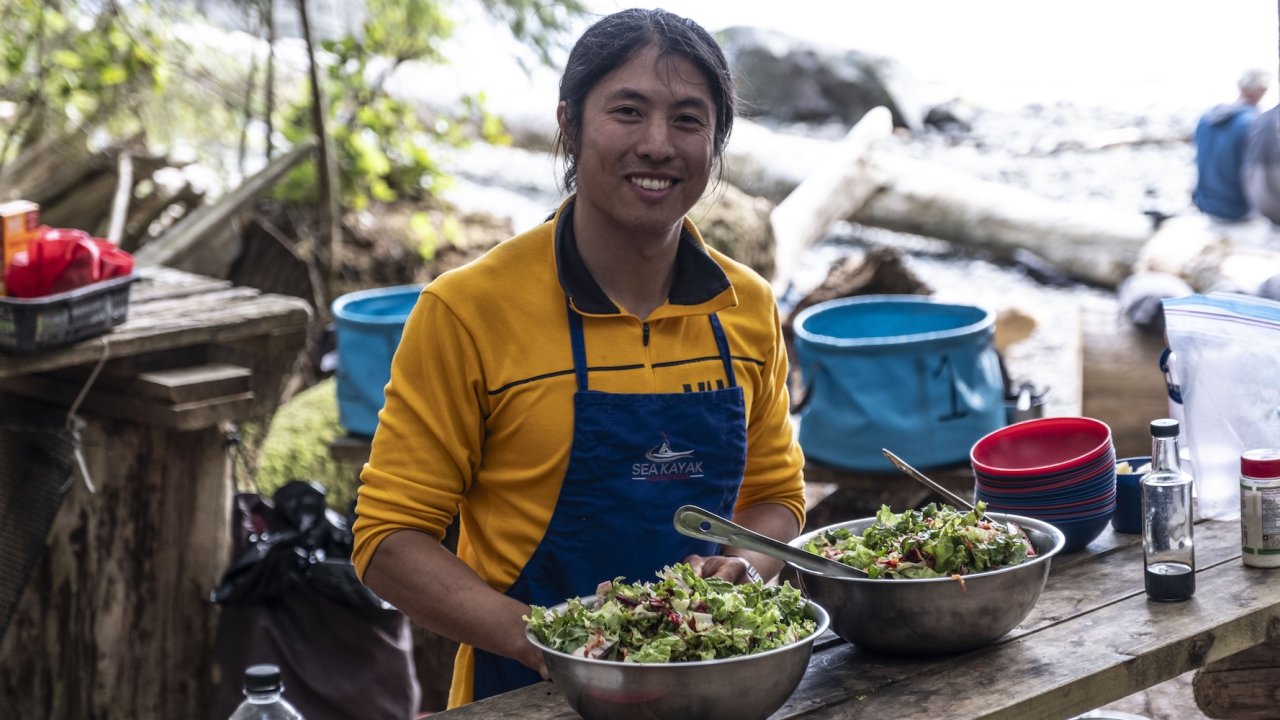 Sea Kayak Adventures guide prepares fresh salad at a rustic camp kitchen in British Columbia.