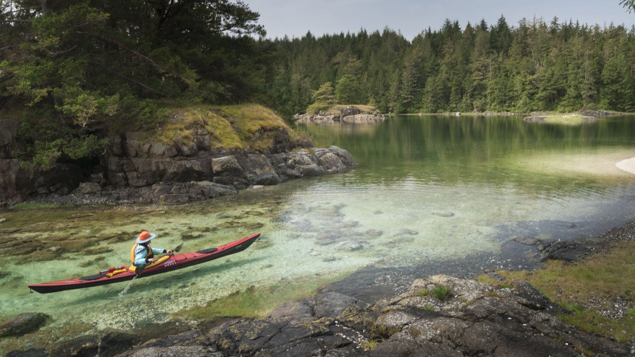 Woman in a single red sea kayak paddling through Johnstone Strait in British Columbia