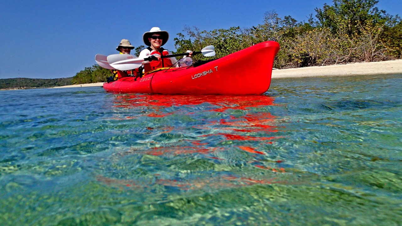 A red tandem sea kayak with people paddling and smiling off the shores of Cuba
