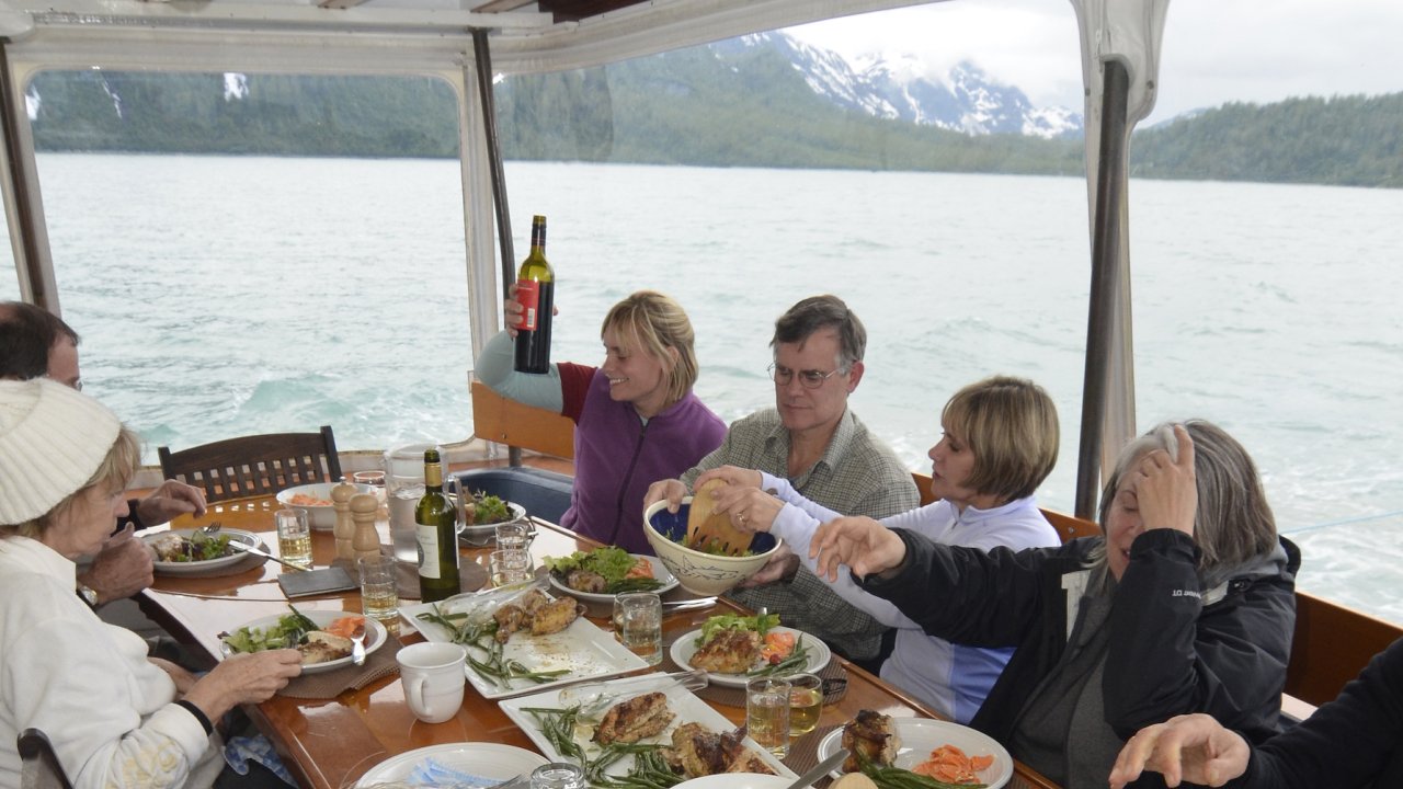 People sitting around the dinner table in a dining room lined with windows on a boat in Alaska