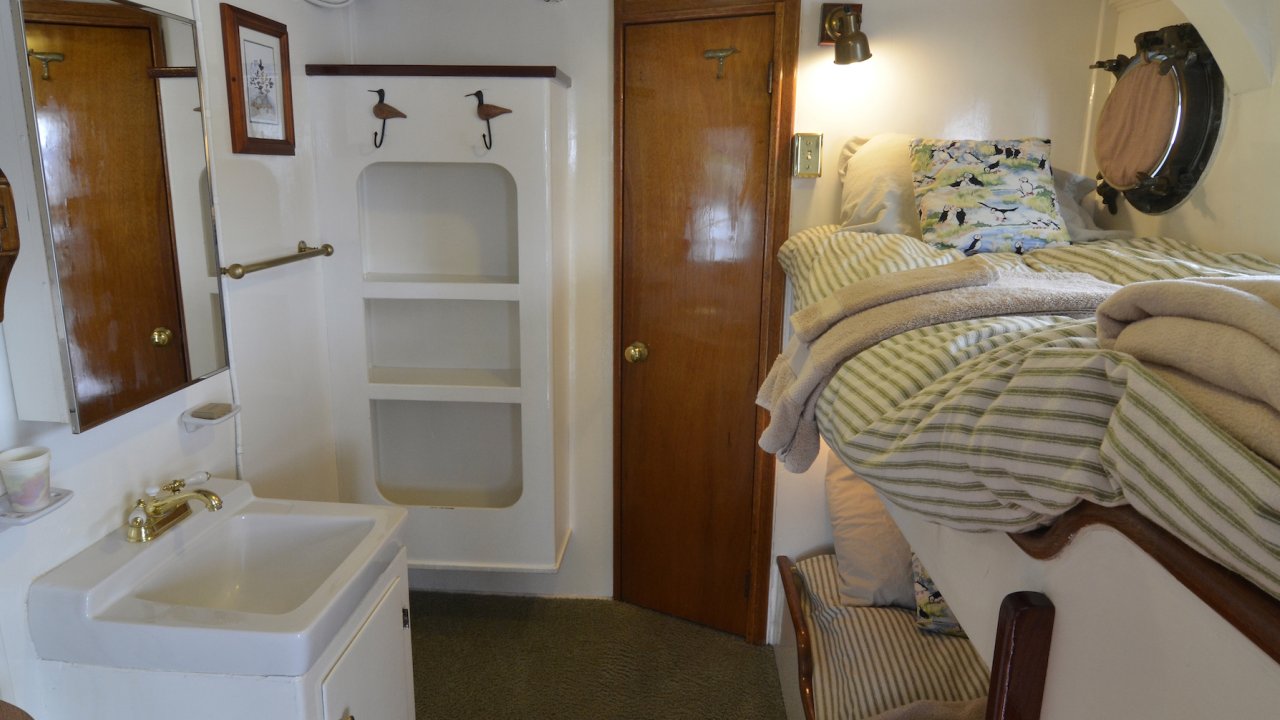 Twin bunk beds with freshly folded towels and a sink in the Sea Wolf Boat single stateroom