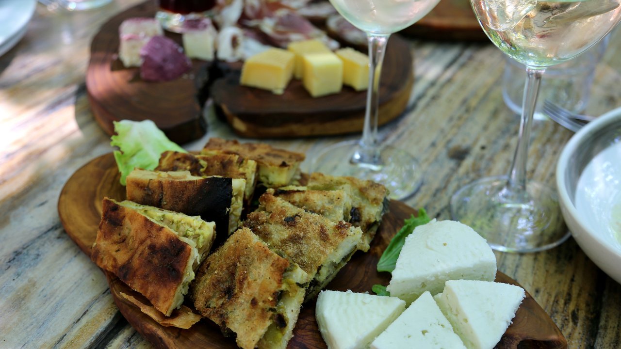 Traditional Albanian food on a cutting board with two wine glasses