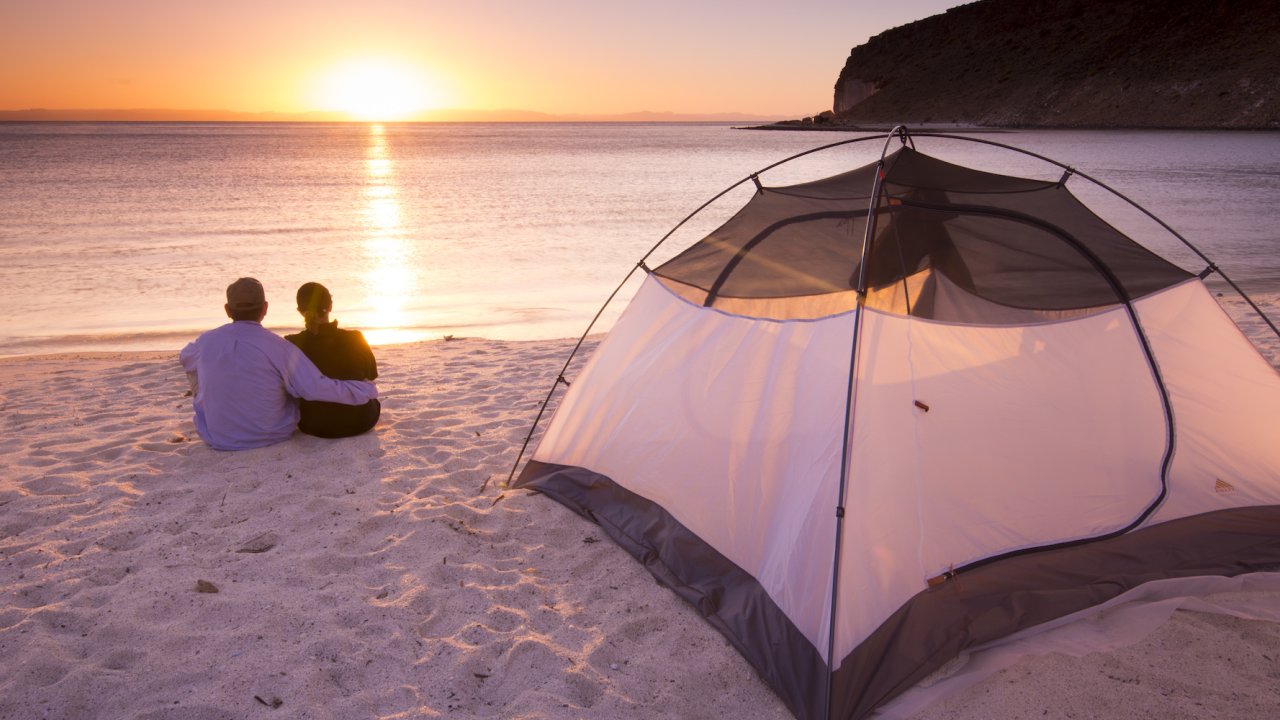 A couple sitting in the sand in front of their tent at sunset in La Paz