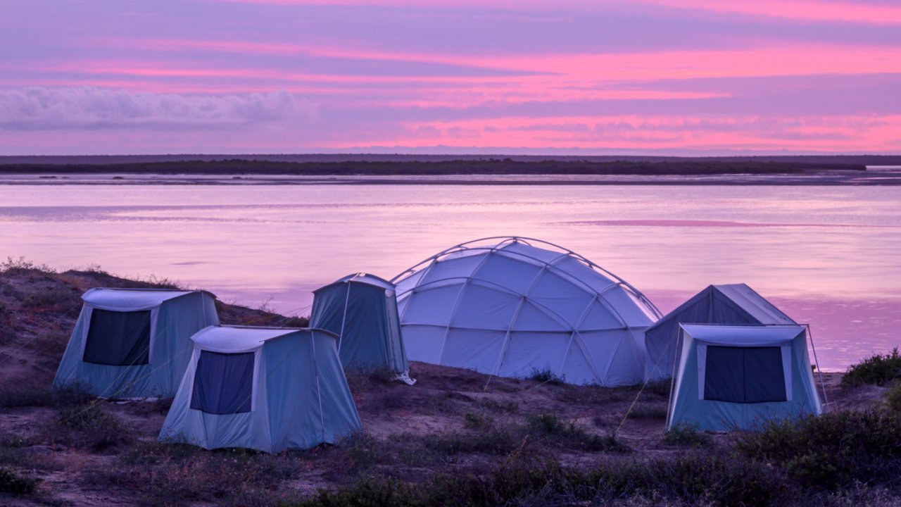 High wall canvas tents lined up on a beach at sunset