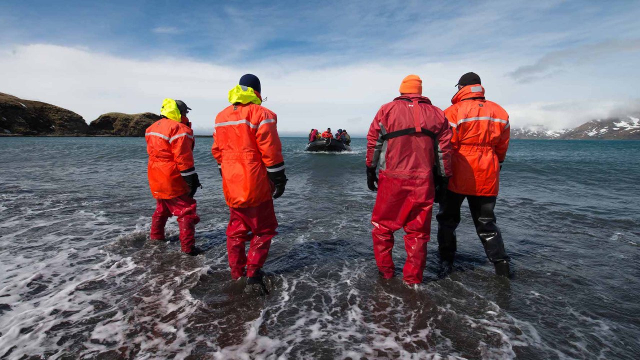 4 people in protective suites walking through the water to get back to their raft in Antarctica