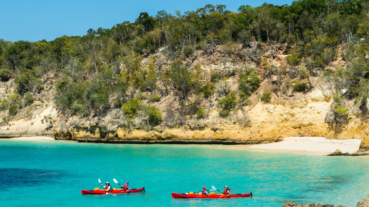 Two red tandem sea kayaks on the water paddling towards shore among cragged cliffs in Cuba on a sunny day