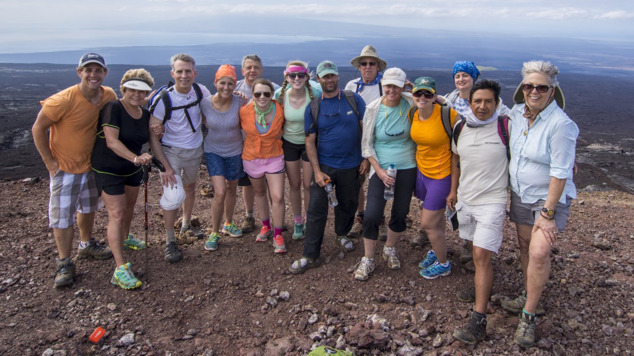 A group of travelers on a guided Galapagos tour at the top of a volcano hike smiling together