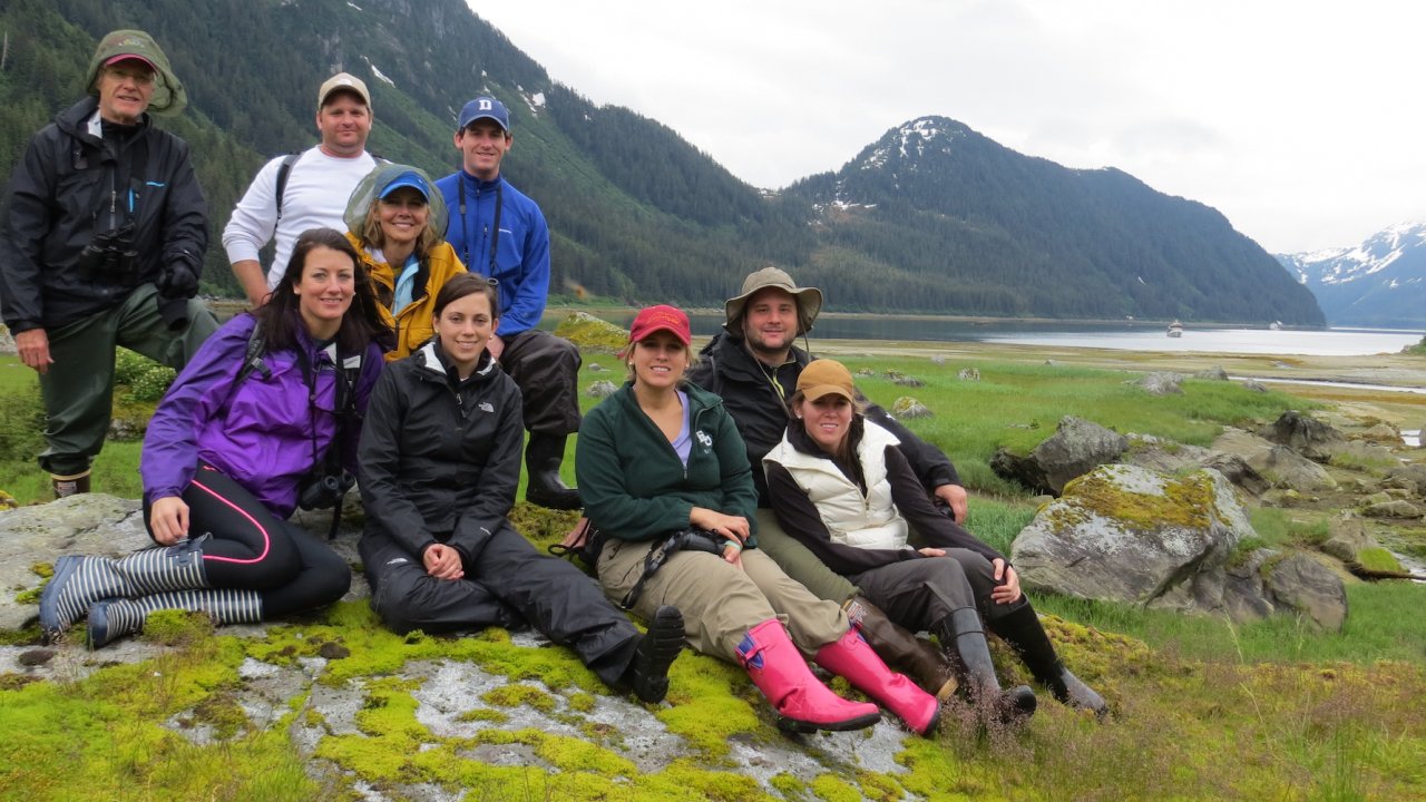 A group of hikers sitting and standing on a rock in a green grass field on a misty day in Alaska