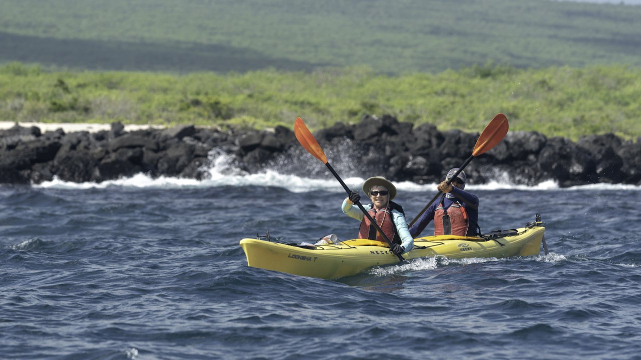 A couple smiling and paddling in a yellow tandem sea kayak in the Galapagos Islands