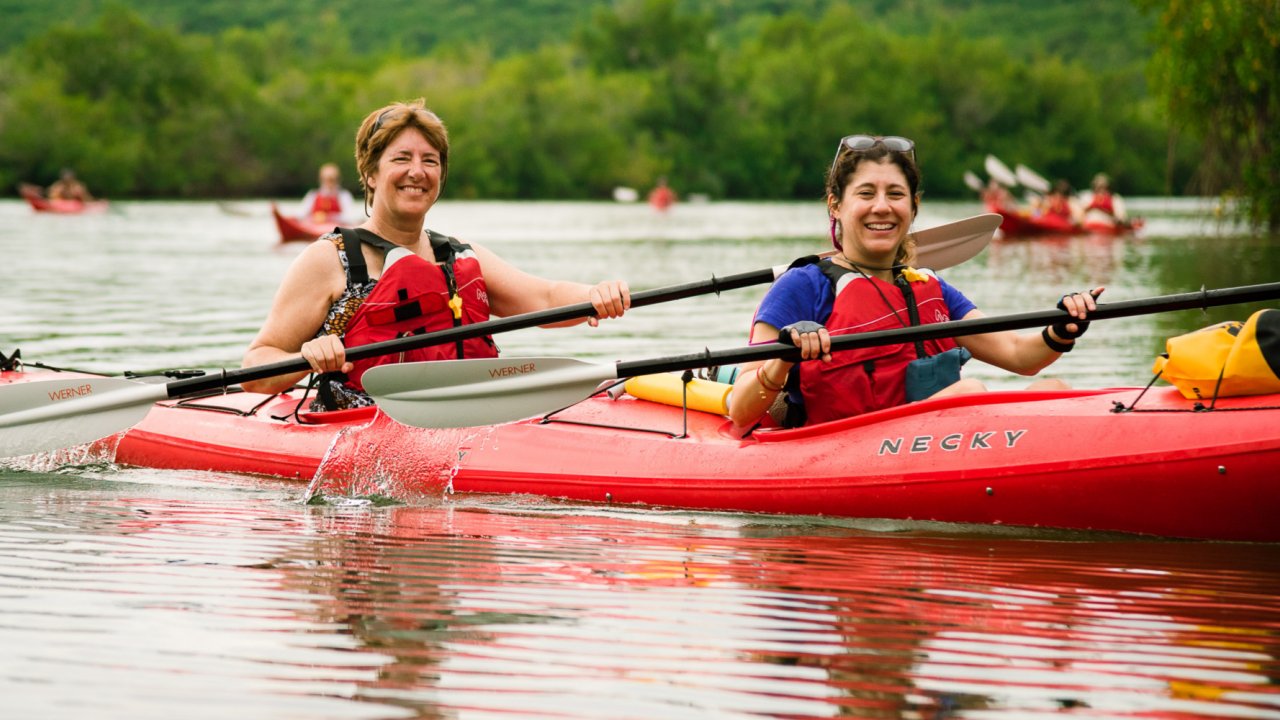 Two women in a red tandem kayak smiling for the camera while paddling in Cuba