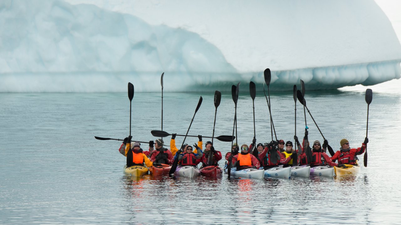  A group of sea kayakers holding up their paddles in Antarctica