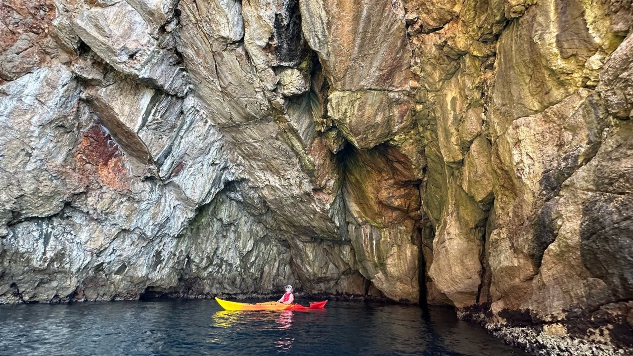 A sea kayaker in Europe exploring a rocky cliffside.