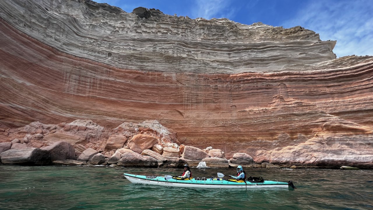 Tandem sea kayakers off the coast of La Paz paddling by a beautiful sandstone scape wall