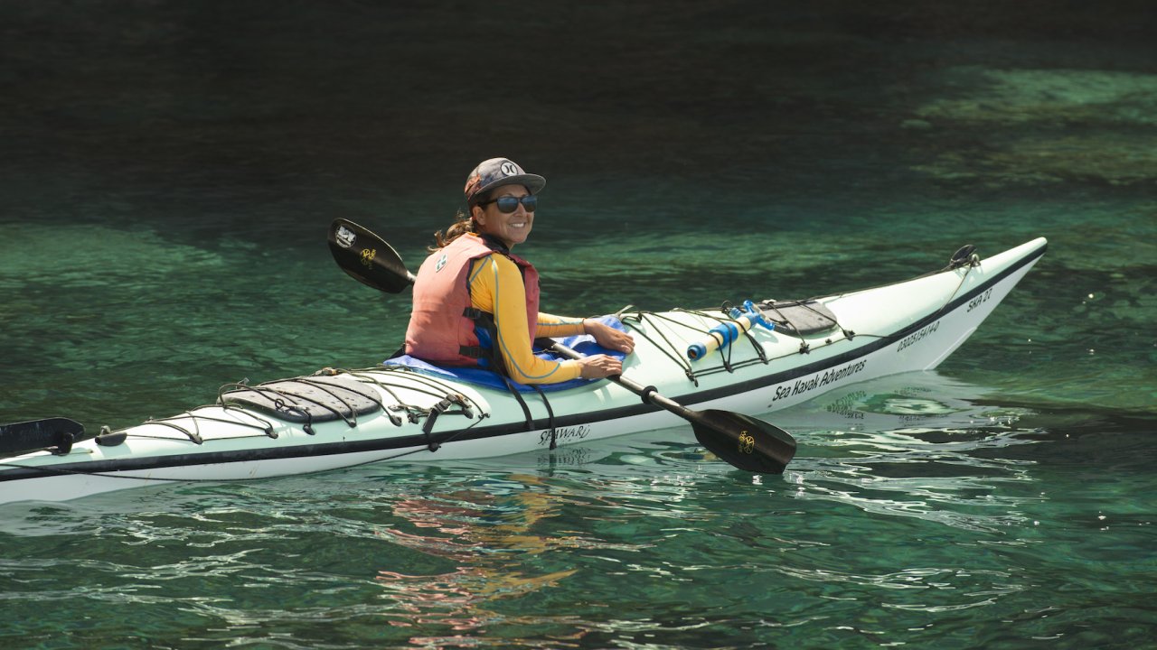 A kayaker in a single kayak paddling and smiling in Baja