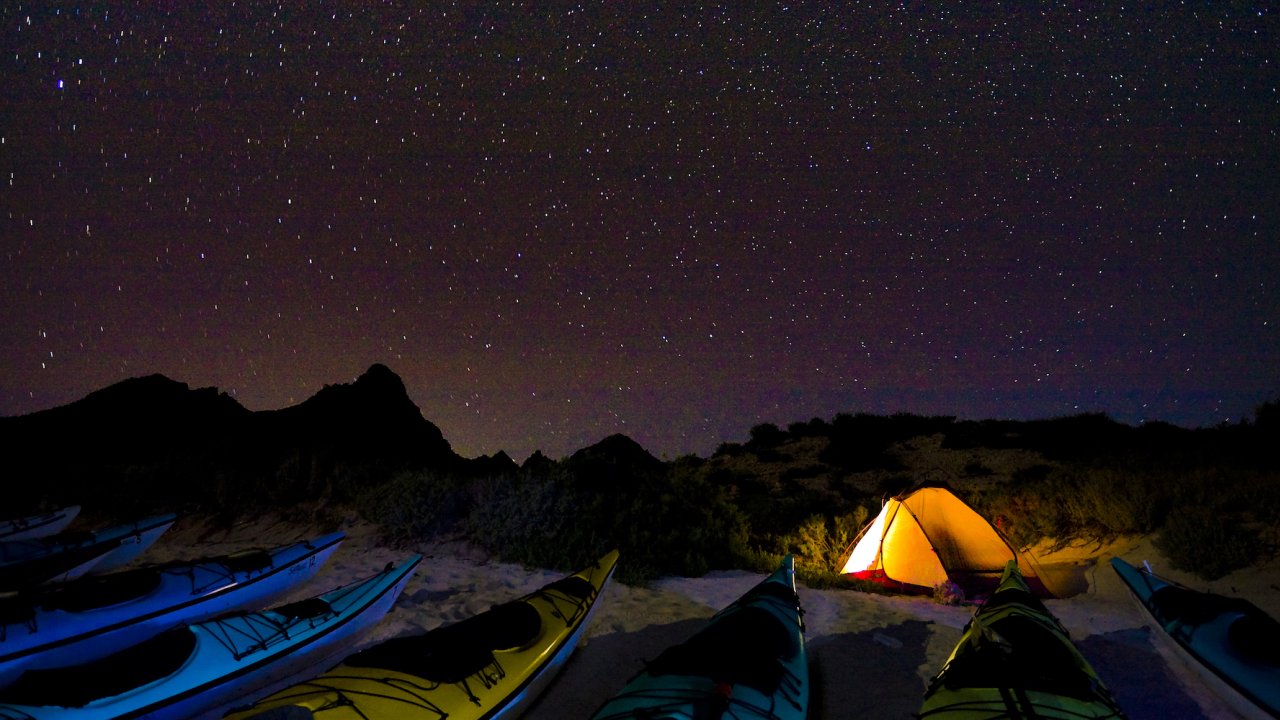 A row of kayaks and a lit up tent under the stars at night