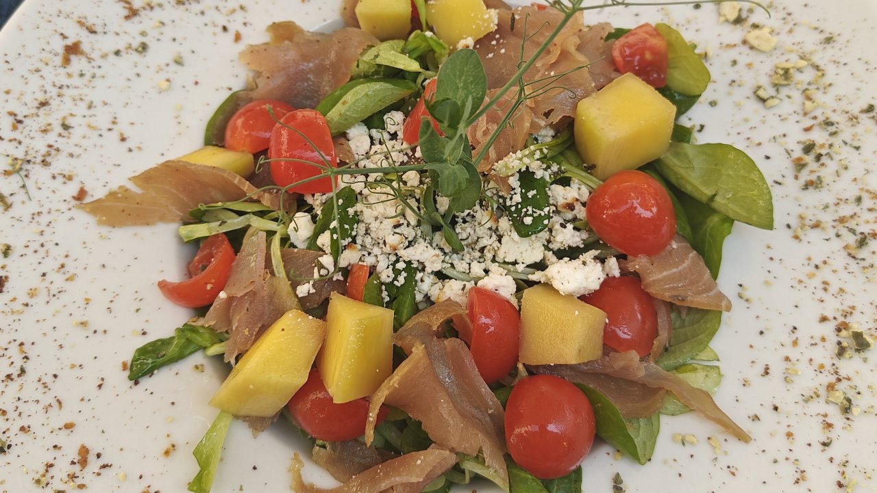 A white dinner plate of arugula, grape tomatoes, and fresh fish 