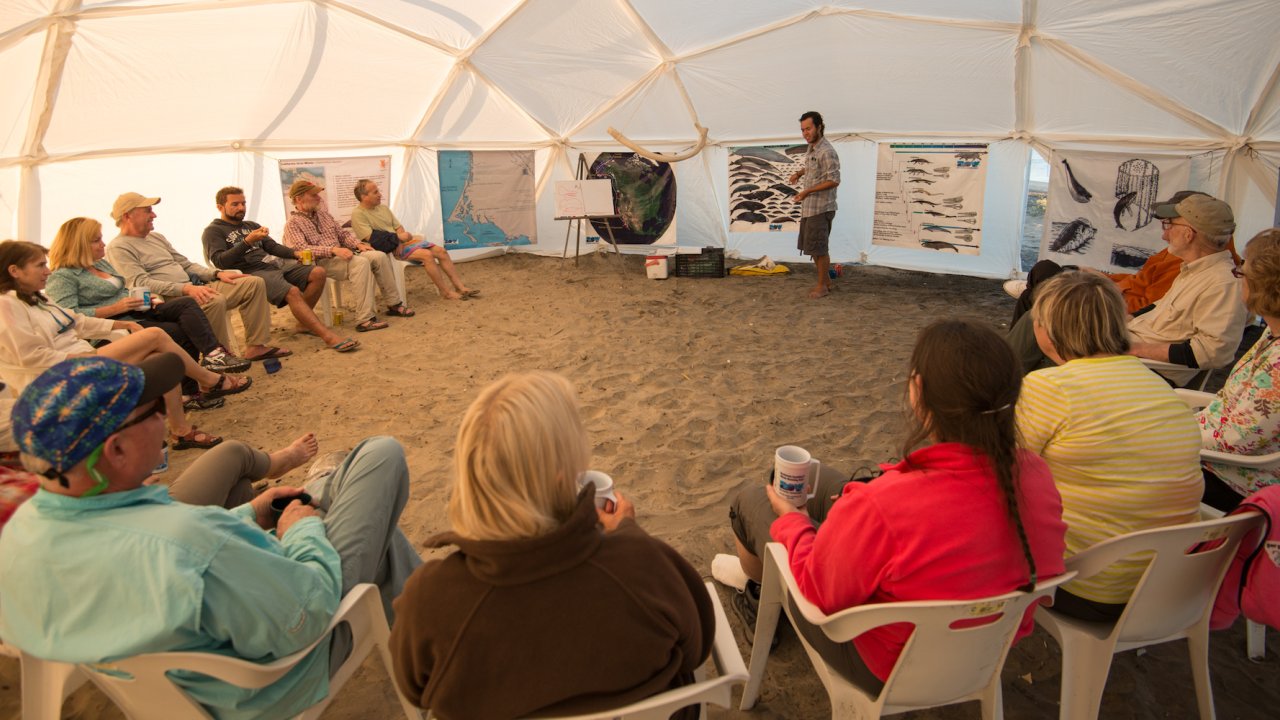 Travelers sitting in a circle inside of a dome tent listening to their guide talk about gray whales