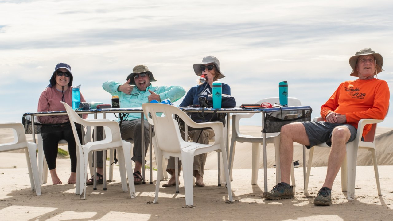 group sitting at camp table on sand