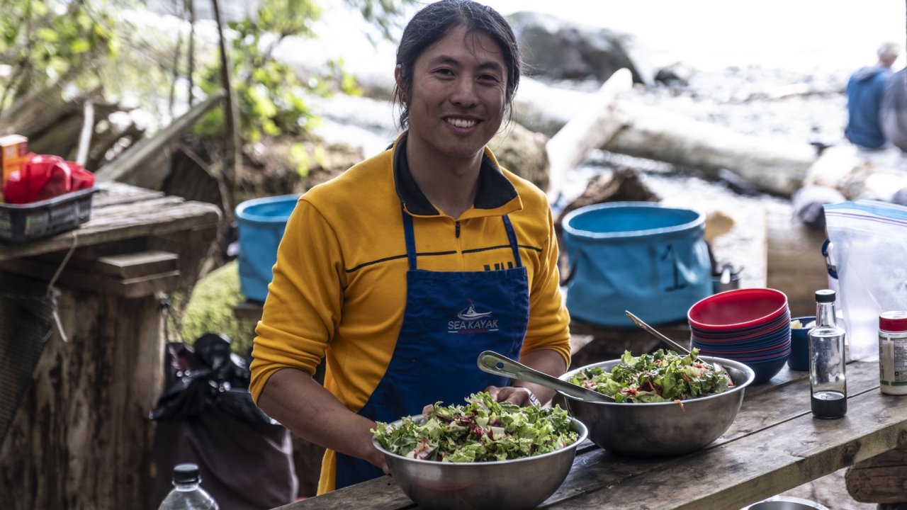 Guide preparing fresh salad at a wilderness kayak camp during a British Columbia orca kayaking tour