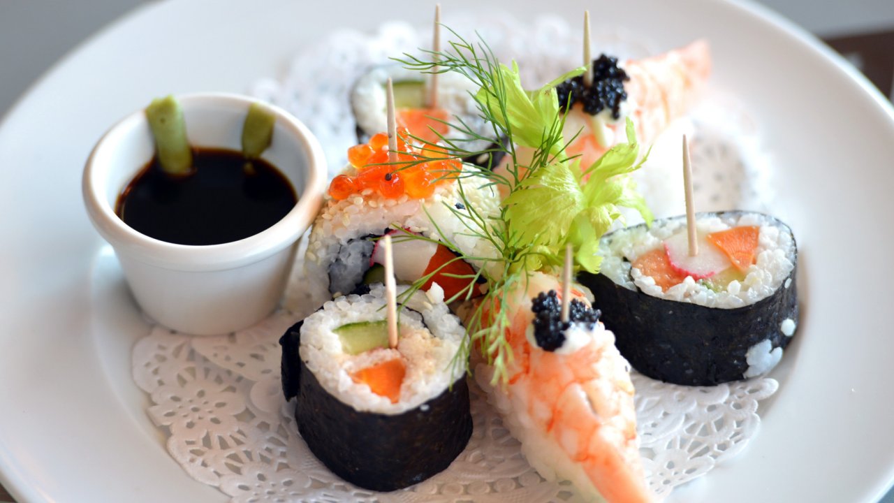 Sushi on a white plat atop a nicely set table with a white table cloth on a small cruise ship 