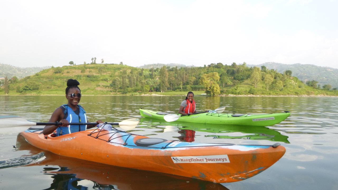 Two travelers kayaking on calm water at Lake Kivu with rolling green hills behind them.