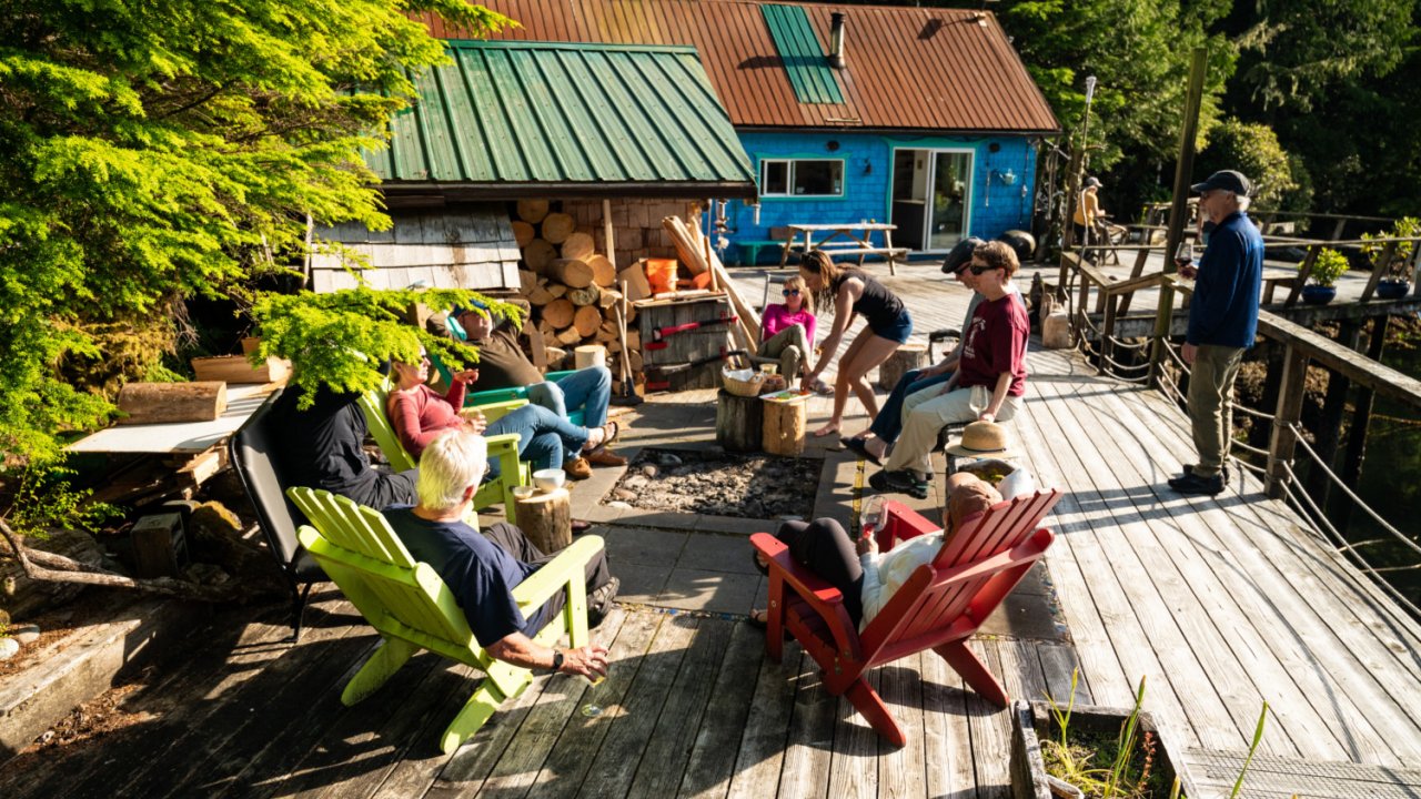 people visiting in chairs and standing on wood deck