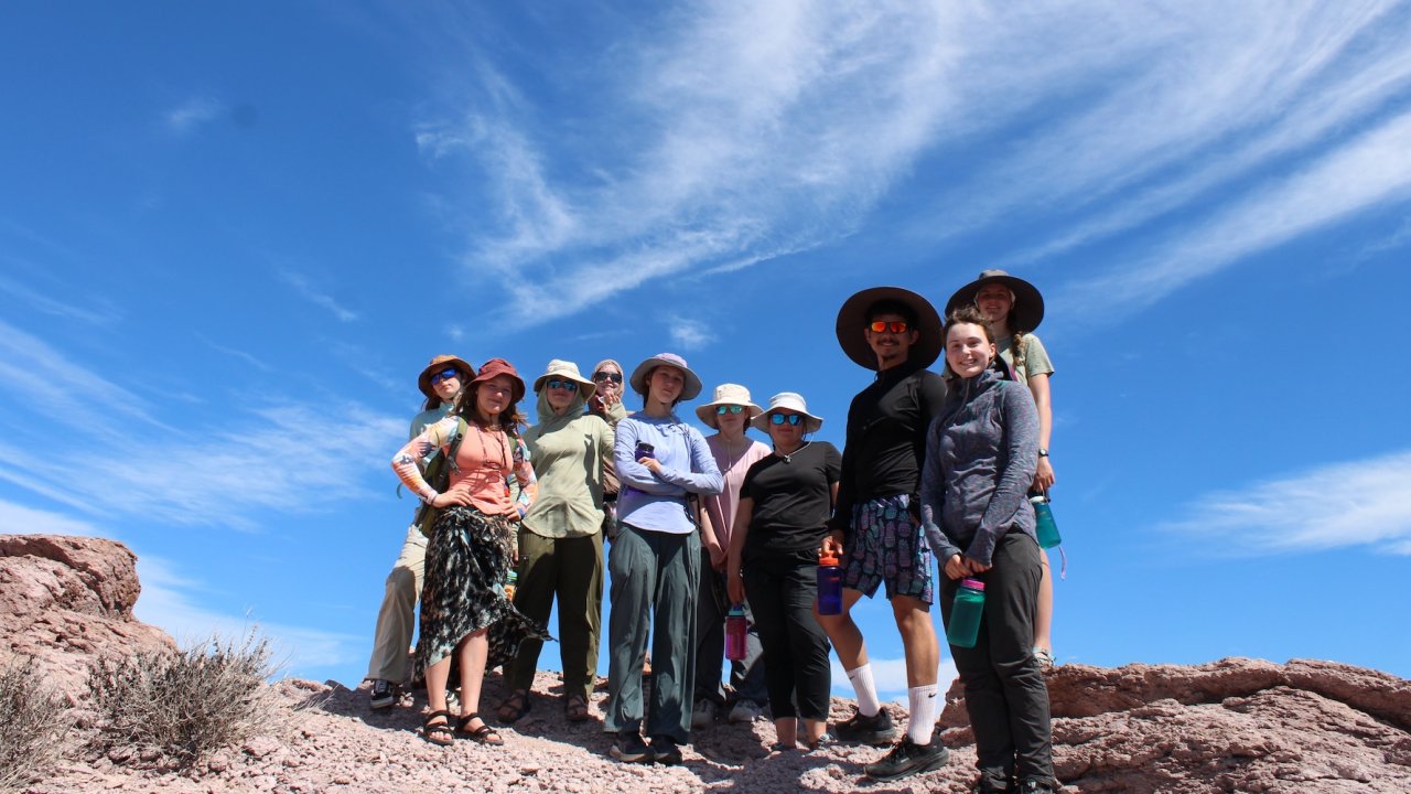 International student travel group posing on a rocky desert overlook under a bright blue sky, taking part in an educational outdoor adventure in Baja California Sur.